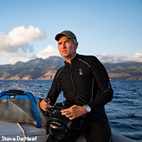 Photo of Brian Skerry wearing a wetsuit on a boat in water with camera ready