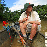 Photo of Zoltan Takacs in a small boat on Amazon River with a colorful parrot riding with him 