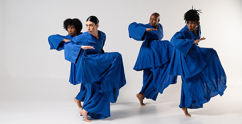 Photo of four Ronald K. Brown dancers in action wearing large oversize blue gowns