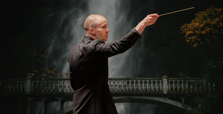 conductor facing right in front of backdrop of darkened photo of a bridge in front of a waterfall