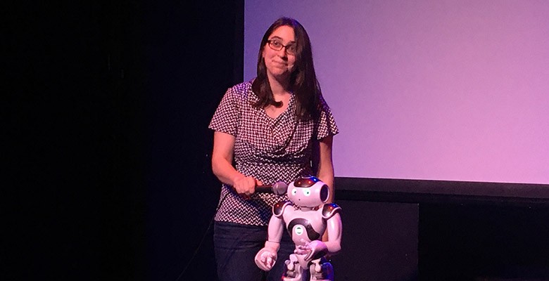 Photo of woman on stage holding microphone up to a robot's face