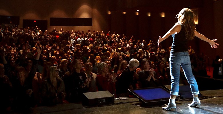 Photo from behind of one of the hosts of We Can Do Hard Things on stage with audience