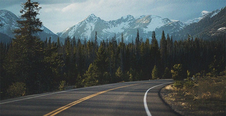 Photo of a curving road with snowy mountain peaks in the background