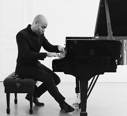Black & white photo of Aaron Diehl playing piano on a white stage.