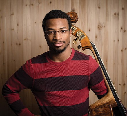 Photo of Xavier Foley holding a double bass against a wood grain background.