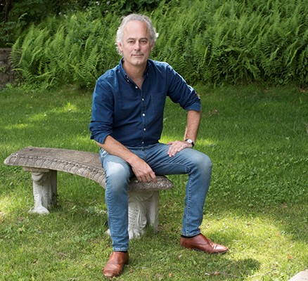 Photo of Amor Towles sitting on a stone bench in green grass by Dmitri Kasterine