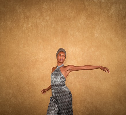 Photo of dancer Catherine Ellis Kirk wearing silver dress against a light brown background/wall