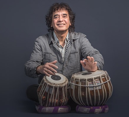 Photo of Zakir Hussain sitting playing drums with his hands
