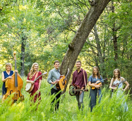 Photo of The Petersens band members holding instruments in a nature setting with trees and grass