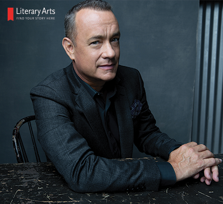 Photo of Tom Hanks sitting at a table, wearing a dark suit