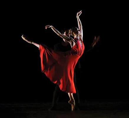 Photo of dancer wearing red dress in pose with black background