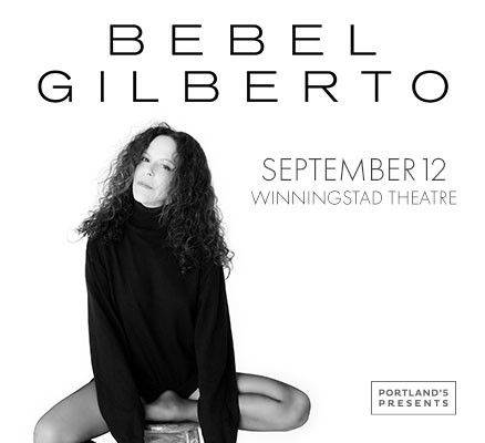 Black and white photo of Bebel Gilberto sitting on a stool with name in text