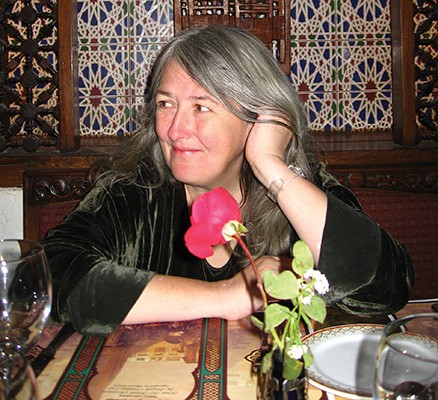 Photo of Mary Beard sitting at a restaurant table, looking to side, smiling