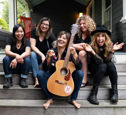 Photo of Ashley Flynn & The Riveters sitting together on porch steps, smiling