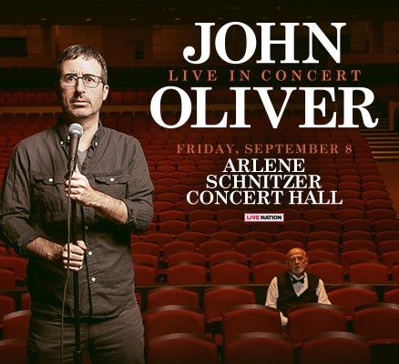 John Oliver holding a microphone in an empty theatre