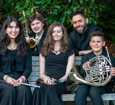 Photo of MYS musicians sitting on bench with conductor standing behind them