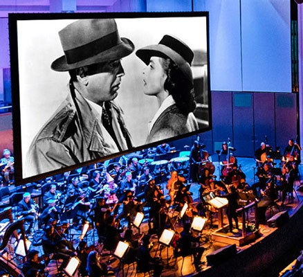 Scene from Casablanca on movie screen with symphony playing below/in front