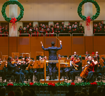 symphony and choir performing on stage with holiday garland
