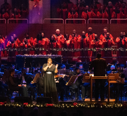 gospel singer and choir on stage with seated symphony players surrounded by holiday garland