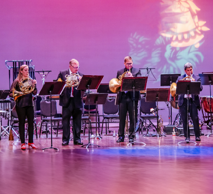 brass players standing on stage in front of purple backdrop