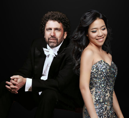 curl haired man in tux looking at camera brown haired woman in sparkly dress looking down to right