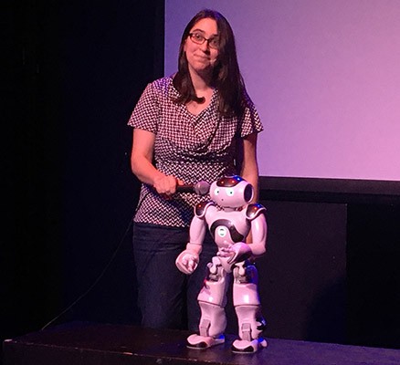 Photo of woman on stage holding microphone up to a robot's face