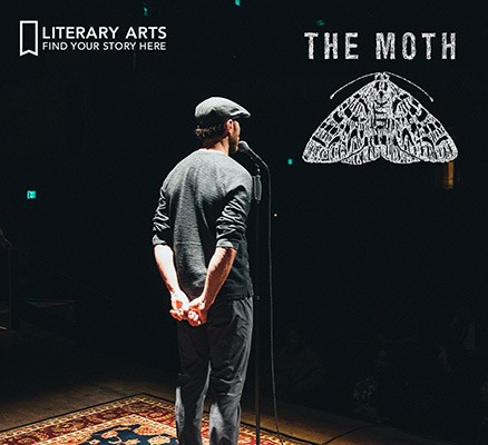 Photo of The Moth performer on stage (from behind) standing at microphone