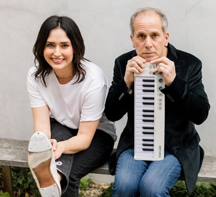 A photo of Larry Golding sitting with a small keyboard on the right and dancer Melinda Sullivan holding a foot up to the camera on the left