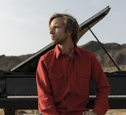 Metropolitan Youth Symphony presents Hunter Noack - photo of Hunter sitting with his back to a grand piano outdoors