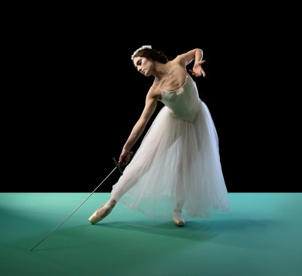 Photo of a solo dancer on a darkened stage posing in a spotlight