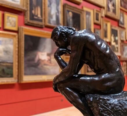 Image of bronze statue of man sitting and framed paintings in background