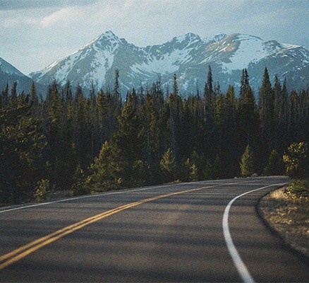 Photo of a curving road with snowy mountain peaks in the background