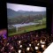 Photo of scene from Jurassic Park shown on screen with symphony performing
