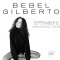 Black and white photo of Bebel Gilberto sitting on a stool with name in text