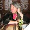 Photo of Mary Beard sitting at a restaurant table, looking to side, smiling