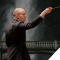 conductor facing right in front of backdrop of darkened photo of a bridge in front of a waterfall