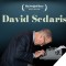 Photo of David Sedaris sitting with head down over typewriter, typing