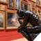 Image of bronze statue of man sitting and framed paintings in background